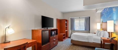 Quarto de hotel com cama, escrivaninha, televisão e um quadro na parede.