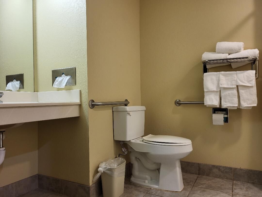 Un baño con inodoro, lavamanos, espejo y toallero con toallas.