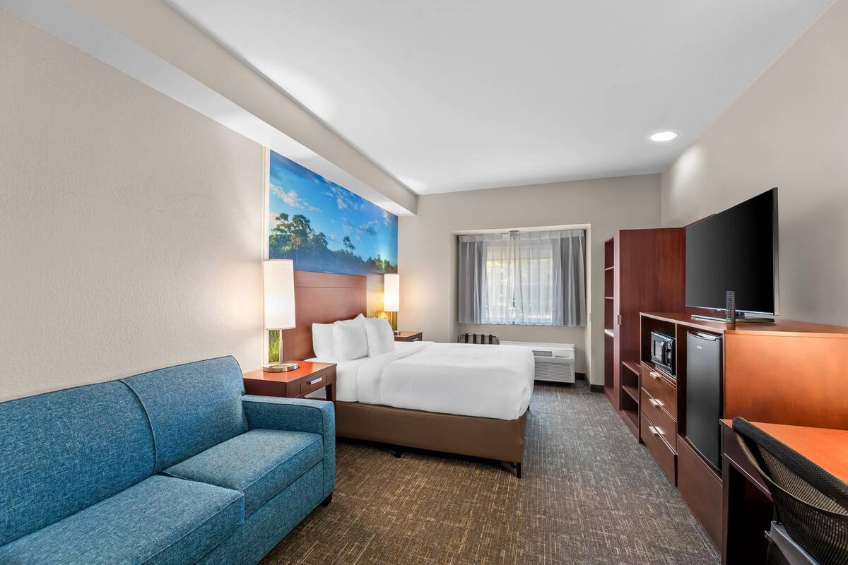 Une chambre d’hôtel avec un lit, un canapé bleu, un bureau, une télévision et un tableau au mur.