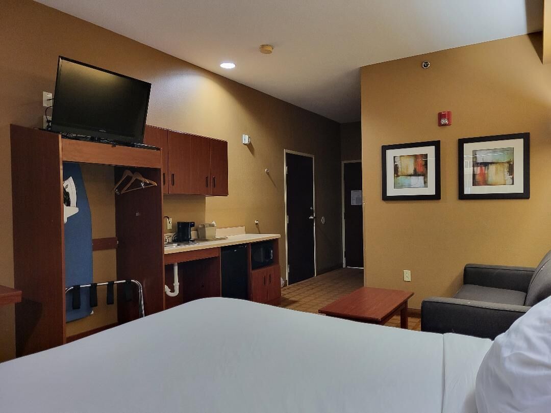 A hotel room with a bed, a desk with a computer, a television, a small table, and two framed pictures on the wall.