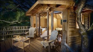 A wooden cabin with a deck, furnished with chairs and a table, and a bed inside. - Agroturismo Mari Cruz (Arce)