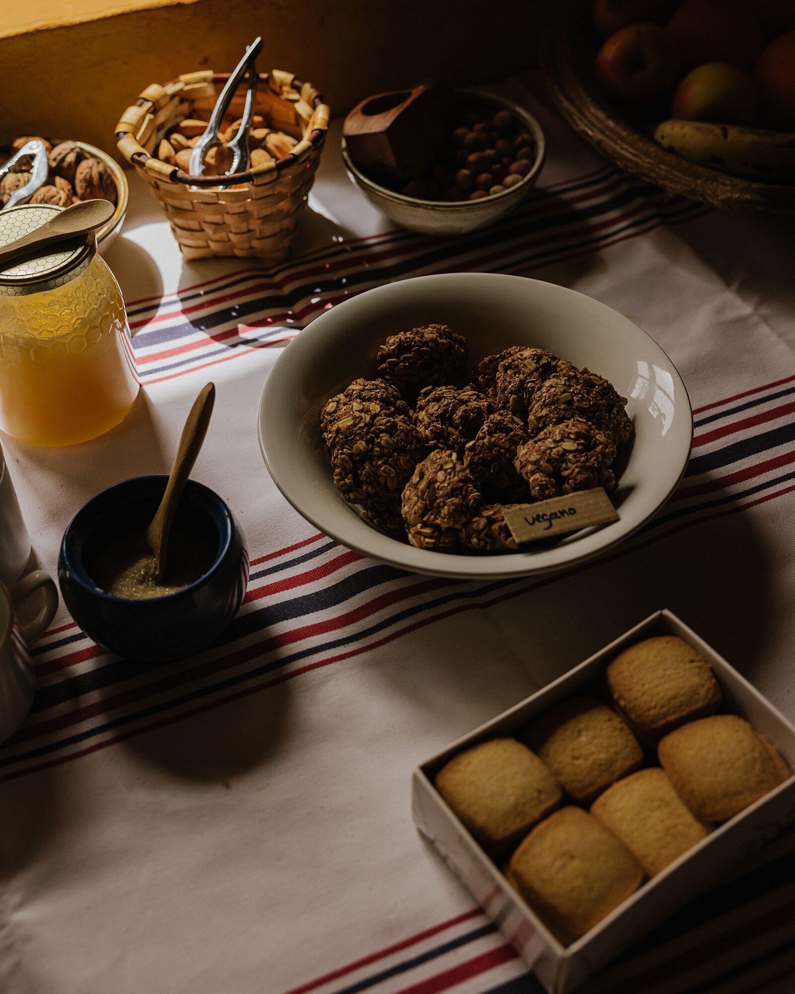 A table with a bowl of granola, a jar of honey, and a box of cookies.