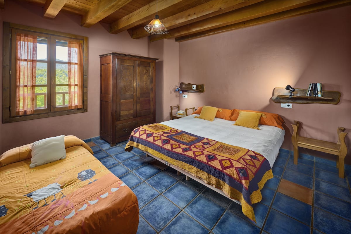 A bedroom with a large bed, a wooden wardrobe, a nightstand, and a window with curtains.