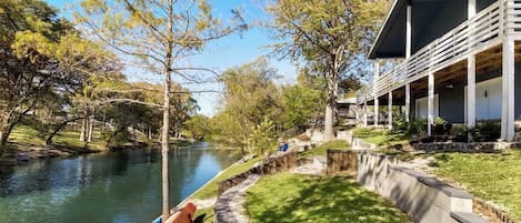 Una propiedad junto al río con un espacio cubierto al aire libre, un sendero y un césped.