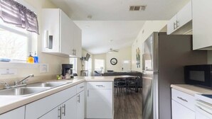 Une cuisine moderne avec des meubles blancs, un réfrigérateur en acier inoxydable et un coin repas comprenant une table et des chaises.