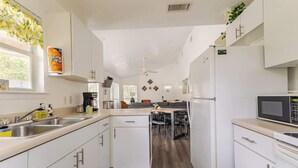 Een moderne keuken met witte kasten, een magnetron, een spoelbak en een eethoek met een tafel en stoelen.