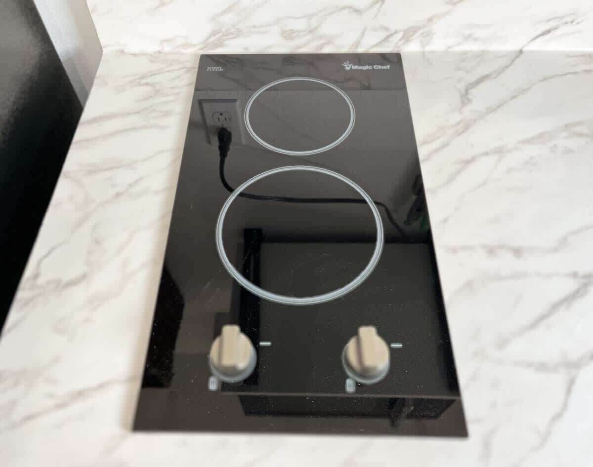 A kitchen with a black countertop, two circular induction cooktops, and two control knobs.