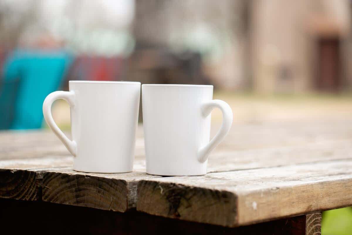 Dos tazas blancas sobre un banco de madera.