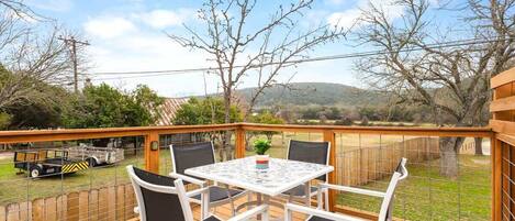 A deck with a table and chairs, overlooking a grassy area and hills.