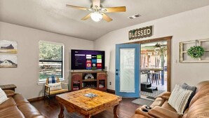Una sala de estar con una mesa de centro de madera, un sofá de cuero, un televisor de pantalla plana y una puerta que dice 'BLESSED'.