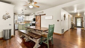 Una cocina amplia con pisos de madera, una mesa de comedor con sillas, un ventilador de techo y un letrero que dice 'FARMER'S MARKET'.