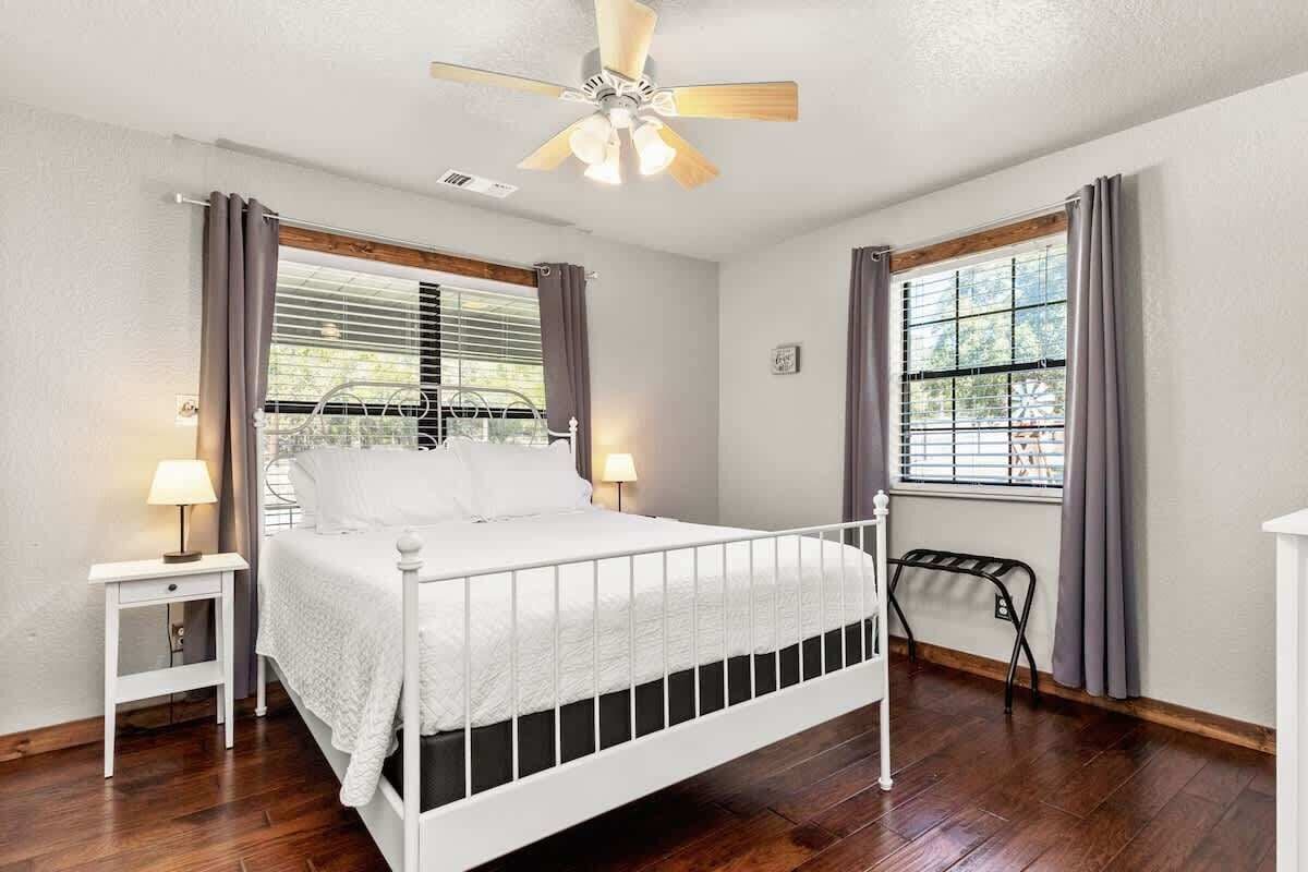 A bedroom with a bed, a nightstand, a ceiling fan, and a window with curtains.