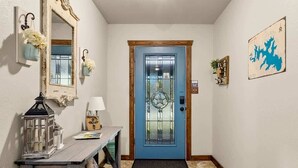 Un pasillo con una puerta azul, un espejo, un farol y una pequeña mesa con una lámpara.