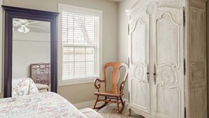 Une chambre à coucher avec un lit, un fauteuil à bascule, une armoire et une fenêtre avec des stores.