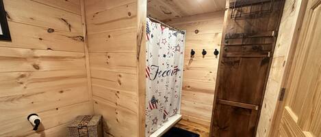 A wooden cabin interior with a shower area, a door, and a small storage box.