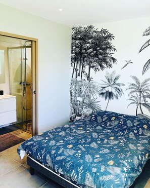 Quarto com cama, chuveiro e um mural de árvores tropicais.
