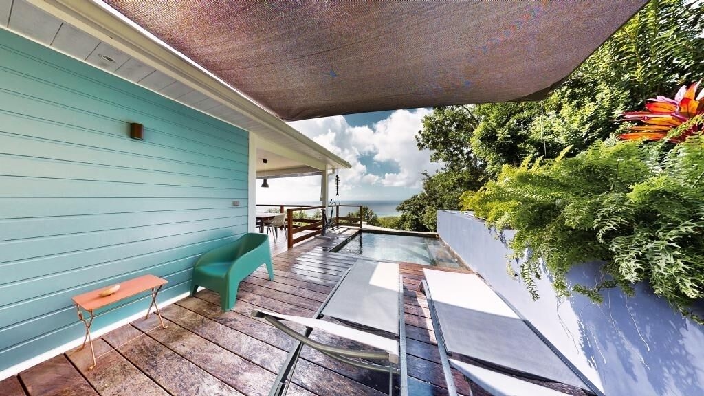 Ein überdachter Außenbereich mit Holzterrasse, einer türkisblauen Wand und Blick aufs Meer.