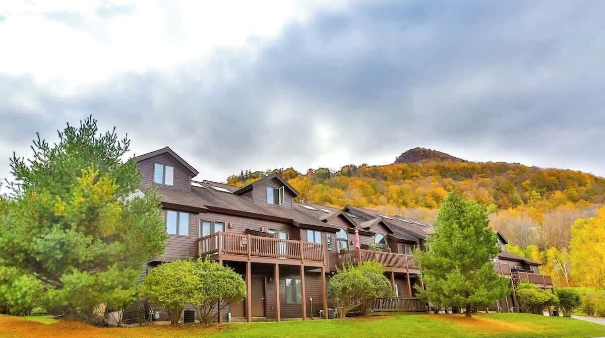 A multi-story building with balconies, surrounded by trees and a hilly landscape.
