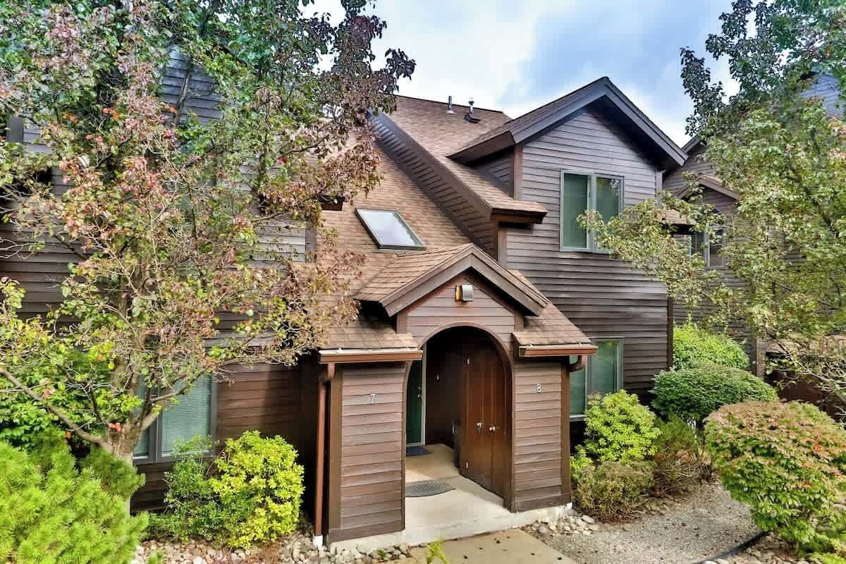 Une maison à deux étages, avec une façade marron, un petit porche à l’avant et un garage.