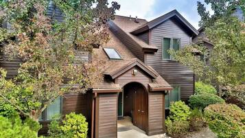 Une maison à deux étages, avec une façade marron, un petit porche à l’avant et un garage.