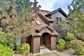 Une maison à deux étages, avec une façade marron, un petit porche à l’avant et un garage.