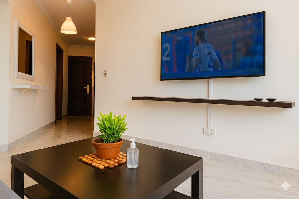 A modern hotel room with a TV mounted on the wall, a potted plant on the table, and a bottle of hand sanitizer.