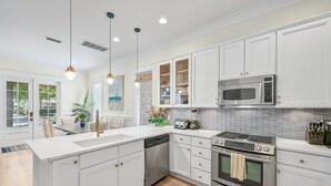 Une cuisine moderne avec des meubles blancs, des appareils en acier inoxydable et des luminaires suspendus.