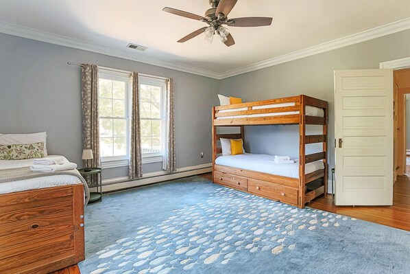 A bedroom with two bunk beds, a wooden dresser, a ceiling fan, and a window with curtains.