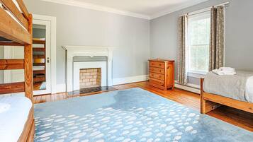 A bedroom with a bunk bed, a fireplace, a dresser, and a window with curtains.