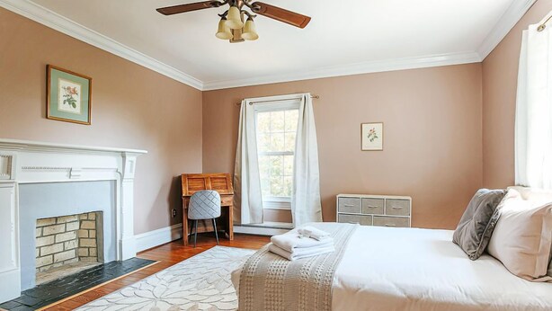 Une chambre avec une cheminée, un lit, un bureau et une fenêtre avec des rideaux.