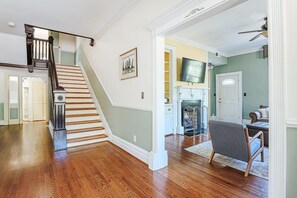 A spacious living area with hardwood flooring, a staircase with a dark wooden handrail, and a gray armchair. - Clonmel Acres: Historic Estate with Hot Tub & Pond (Afton)