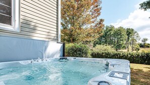 Un bain à remous dans un jardin, avec une maison et des arbres en arrière-plan.