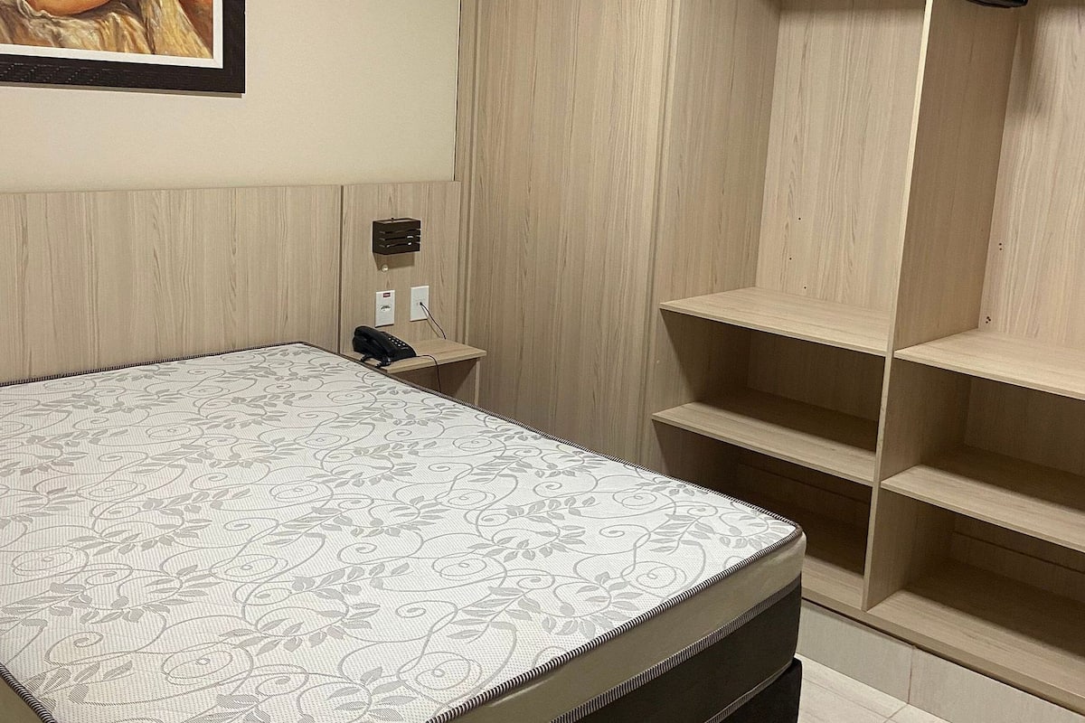 Une chambre à coucher avec un lit, une armoire, une table de chevet, un téléphone et un tableau accroché au mur.