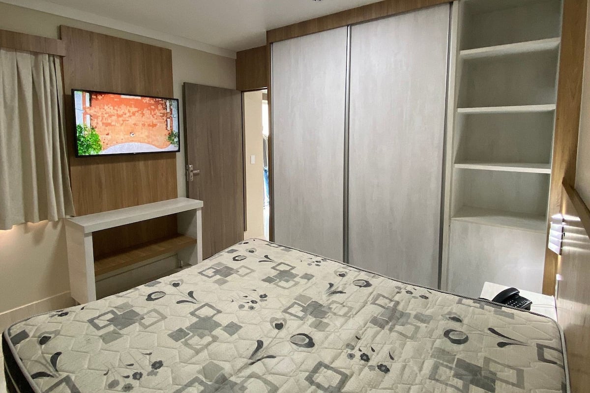 Une chambre à coucher comprenant un lit, un téléviseur fixé au mur, une armoire et un bureau.