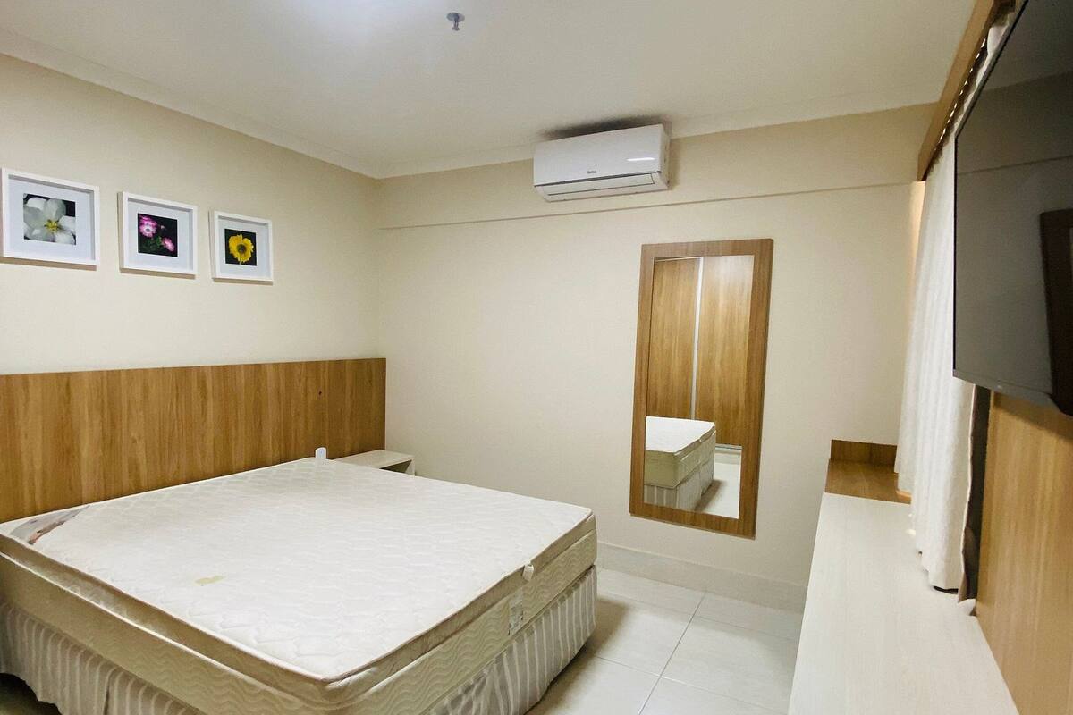 Une chambre à coucher comprenant un lit, un luminaire au plafond, un climatiseur, un miroir et des tableaux encadrés accrochés au mur.