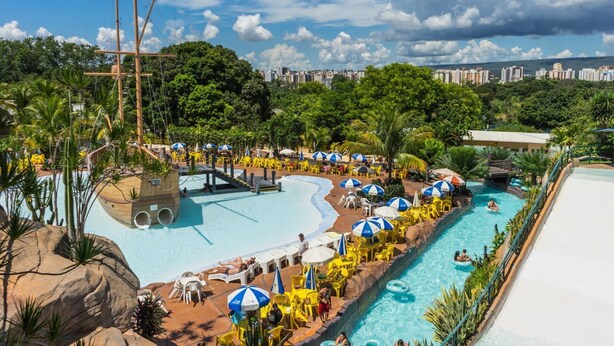 A large outdoor swimming pool with multiple lanes, surrounded by yellow lounge chairs and blue umbrellas. - Condomínio Piazza diRoma Acqua Park Splash (Caldas Novas)