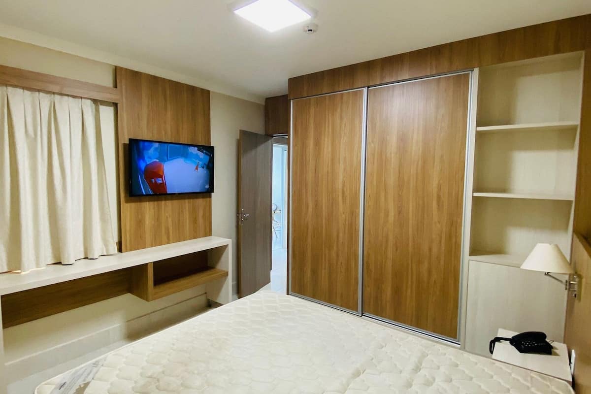 Une chambre d’hôtel avec un grand lit, un téléviseur fixé au mur, des armoires en bois et une table de chevet avec une lampe.
