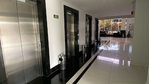 A modern hotel corridor with three elevators, a trash bin, and a clean, tiled floor. - Condomínio Piazza diRoma Acqua Park Splash (Caldas Novas)