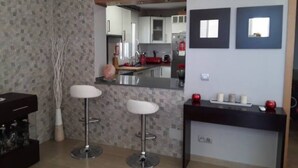 A modern kitchen with a central island, two bar stools, a dining table, and a small seating area with a vase. - Ruhiges und Sonniges Haus in Paguera (Peguera)