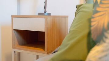 A neatly made bed with a green pillow, a bedside table with a lamp, and a wooden nightstand.