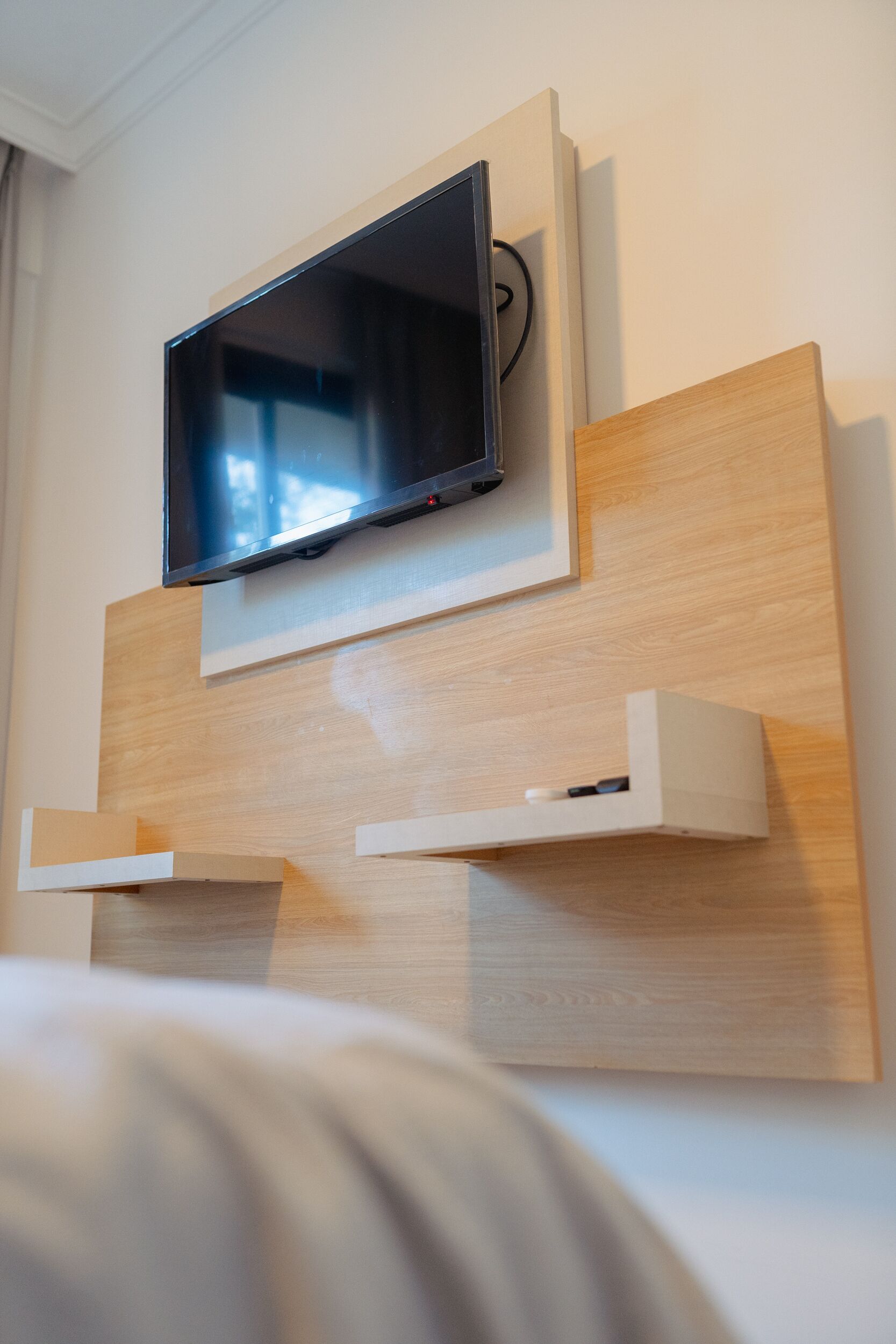 Ein modernes Hotelzimmer mit einem an der Wand befestigten Flachbildfernseher, einer Wandverkleidung aus Holzpaneelen und eingebauten Regalen.