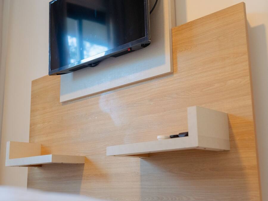 Ein modernes Hotelzimmer mit einem an der Wand befestigten Flachbildfernseher, einer Wandverkleidung aus Holzpaneelen und eingebauten Regalen.
