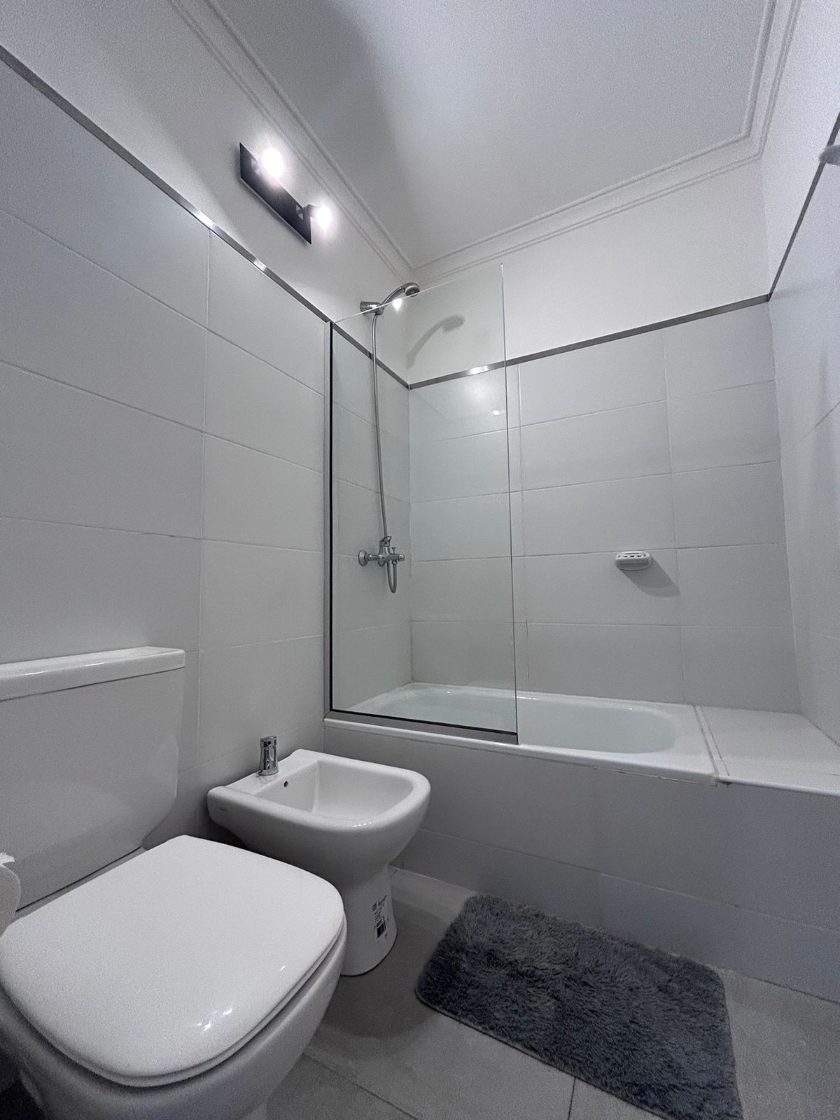 Un baño moderno con inodoro, bidé y zona de ducha con mampara de vidrio.