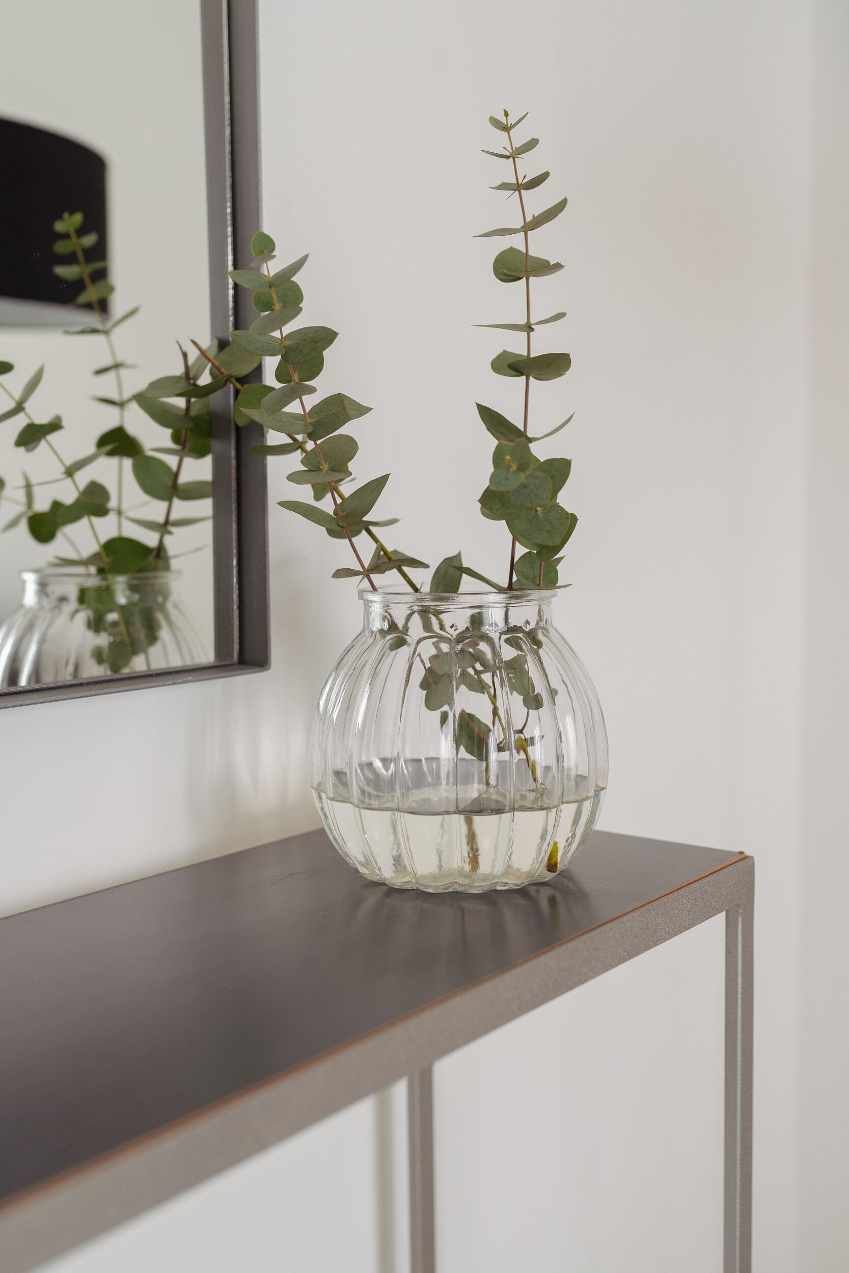 A clear glass vase with water and a plant on a wooden console table.