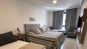 Habitación de hotel con dos camas, un escritorio, una silla, un televisor y una ventana con cortinas.