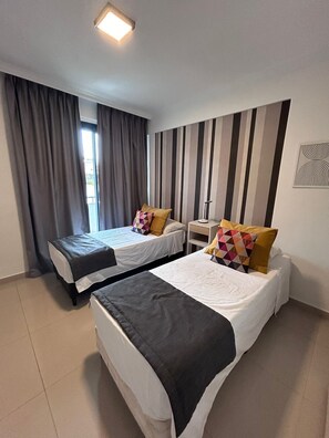 A hotel room with two beds, a nightstand, a lamp, and a striped wall. - Agustín 1 Apart (Parana)