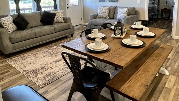 A modern living room with a dining area, a ceiling fan, and a view of the outdoors through large windows. - Relaxing Hillside Getaway with a Mountain View (Franklin)