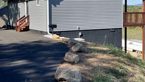 A single-story building with a gray exterior, a covered porch, and a driveway leading to a wooden staircase. - Relaxing Hillside Getaway with a Mountain View (Franklin)