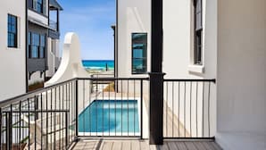 A modern building with a pool, white walls, and a balcony overlooking the ocean.