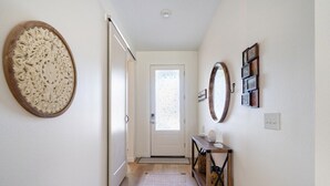 A hallway with a wooden floor, a door at the end, and a console table with a mirror and framed pictures.